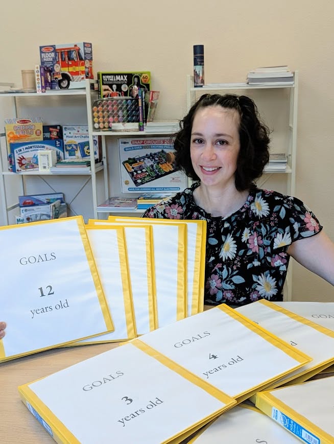 The owner of Hearth & Horizon smiling with her stacks of goals binders